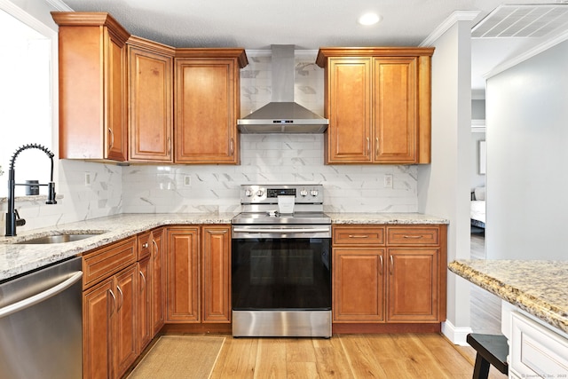 kitchen featuring visible vents, light wood finished floors, a sink, appliances with stainless steel finishes, and wall chimney exhaust hood