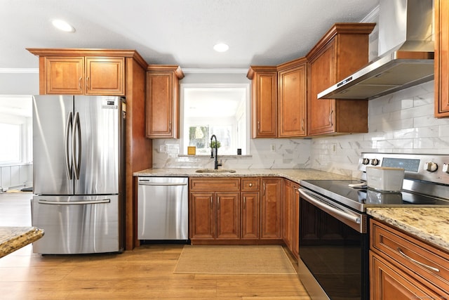 kitchen featuring brown cabinets, light wood-style floors, stainless steel appliances, wall chimney exhaust hood, and a sink