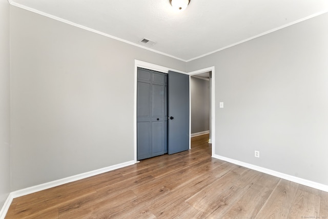 unfurnished bedroom featuring visible vents, light wood-style flooring, ornamental molding, a closet, and baseboards