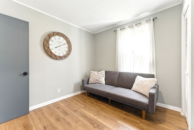 living area featuring baseboards, ornamental molding, and light wood finished floors