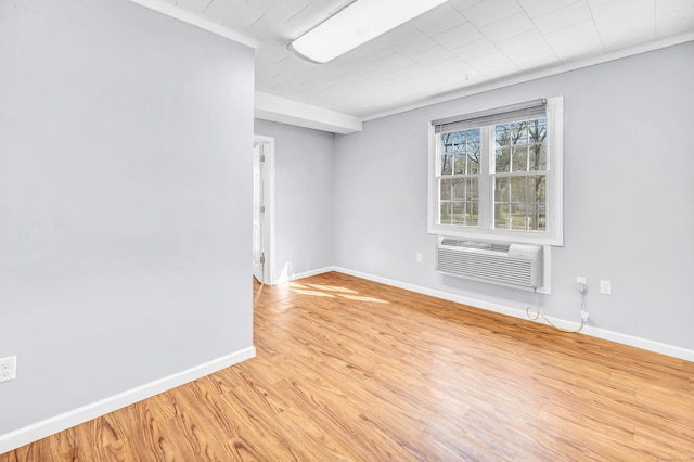 empty room featuring light wood finished floors, a wall mounted air conditioner, crown molding, and baseboards