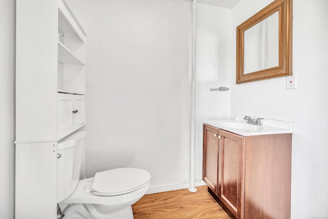 half bathroom with vanity, toilet, wood finished floors, and baseboards