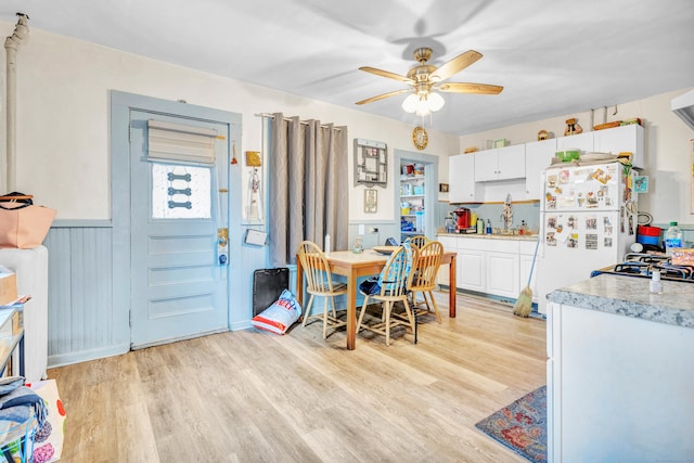 dining area featuring a wainscoted wall, light wood-style floors, and a ceiling fan