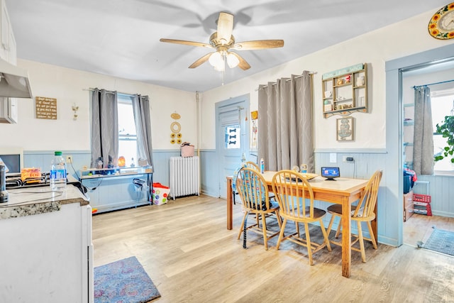 dining room with a wealth of natural light, a wainscoted wall, light wood-style flooring, and radiator heating unit