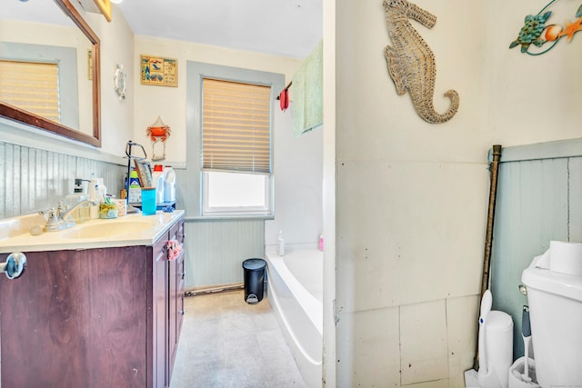 full bath featuring vanity, toilet, a bathtub, and wainscoting