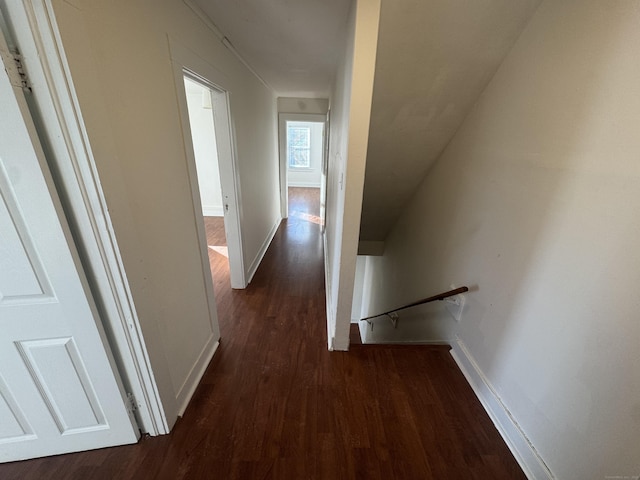 hall with dark wood-style floors, an upstairs landing, and baseboards