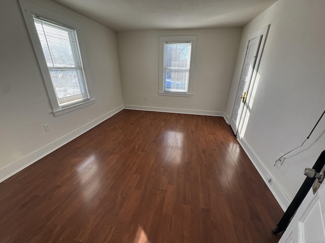 spare room featuring a wealth of natural light, dark wood-type flooring, and baseboards