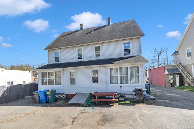 back of property featuring fence, a chimney, and a shingled roof