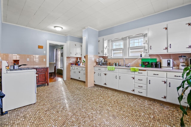 kitchen with white gas stove, ornamental molding, light countertops, white cabinetry, and tasteful backsplash