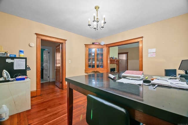 office with baseboards, a notable chandelier, wood finished floors, and a fireplace