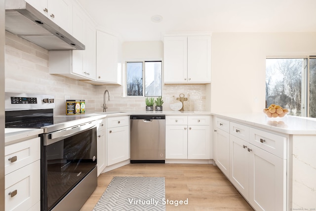 kitchen featuring light wood-type flooring, under cabinet range hood, a sink, appliances with stainless steel finishes, and a peninsula