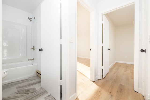 full bathroom featuring a baseboard heating unit, baseboards, wood finished floors, and washtub / shower combination