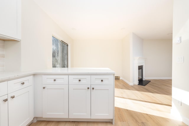 kitchen with light wood-type flooring, light stone counters, a glass covered fireplace, white cabinetry, and a peninsula