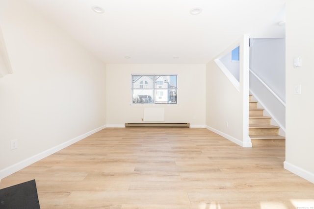 spare room featuring a baseboard heating unit, light wood-style flooring, stairs, and baseboards