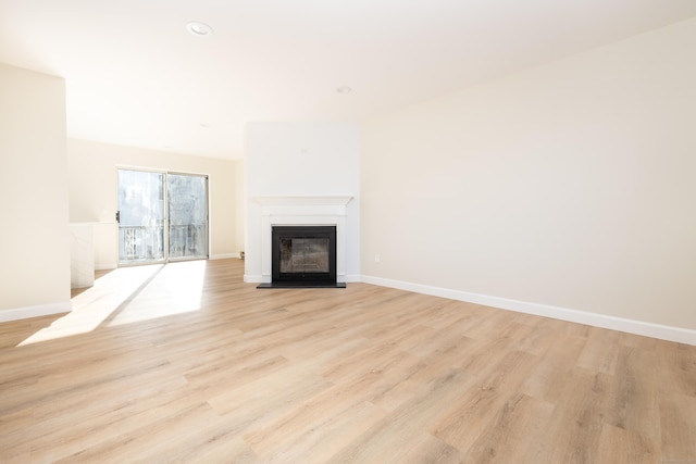 unfurnished living room featuring light wood finished floors, a glass covered fireplace, and baseboards