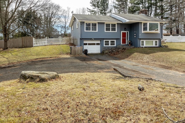 raised ranch with fence, aphalt driveway, a front yard, a chimney, and a garage