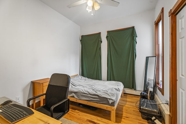 bedroom featuring a baseboard heating unit, a ceiling fan, and wood finished floors