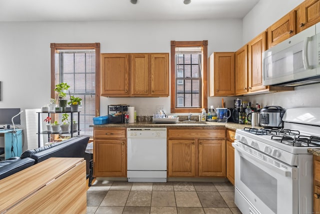 kitchen with a sink, white appliances, brown cabinetry, and light tile patterned floors