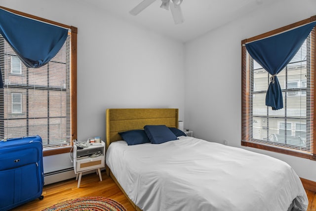 bedroom featuring light wood-style flooring, a baseboard heating unit, and a ceiling fan