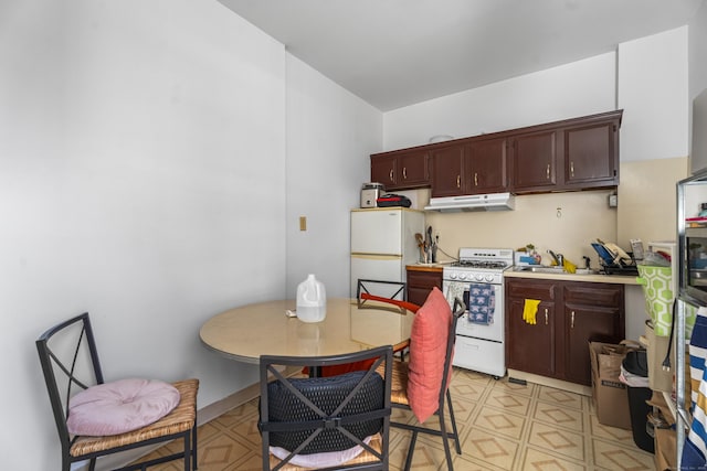 kitchen featuring under cabinet range hood, light floors, light countertops, white appliances, and a sink