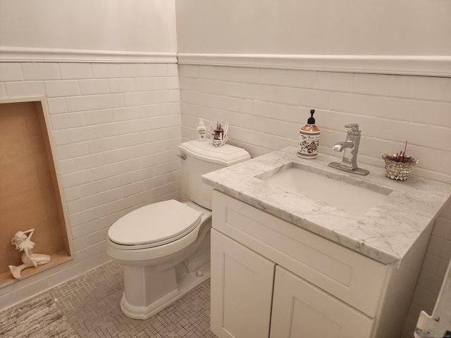 bathroom with tile patterned floors, a wainscoted wall, toilet, tile walls, and vanity