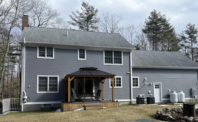 back of house featuring a deck, a gazebo, a yard, a shingled roof, and a chimney