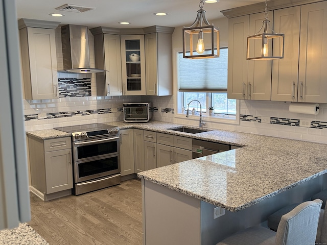 kitchen featuring range with two ovens, visible vents, wall chimney exhaust hood, and gray cabinets