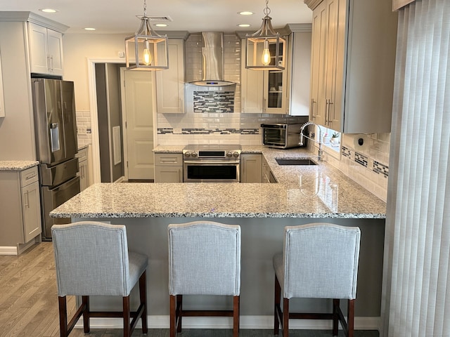 kitchen featuring light wood finished floors, a peninsula, a sink, stainless steel appliances, and wall chimney exhaust hood