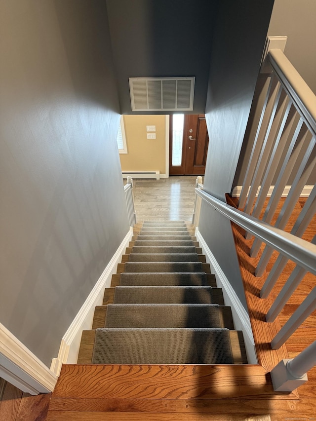 stairs featuring wood finished floors, visible vents, baseboards, and a baseboard heating unit