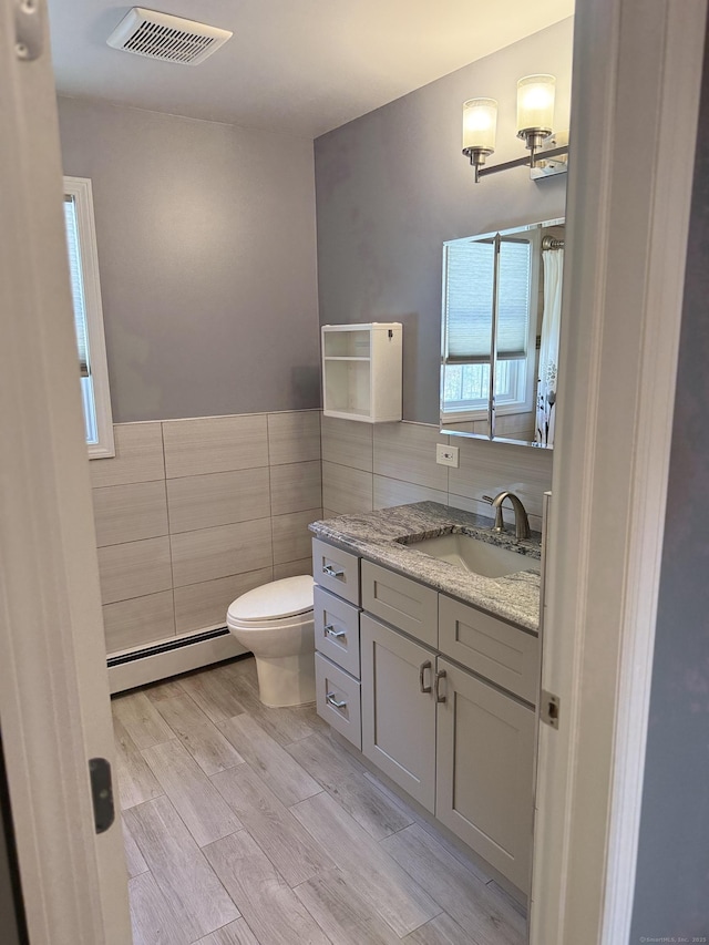 full bath featuring visible vents, toilet, a baseboard heating unit, tile walls, and wood tiled floor