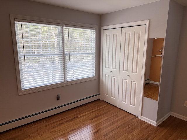 unfurnished bedroom with a baseboard radiator, baseboards, a closet, and wood finished floors