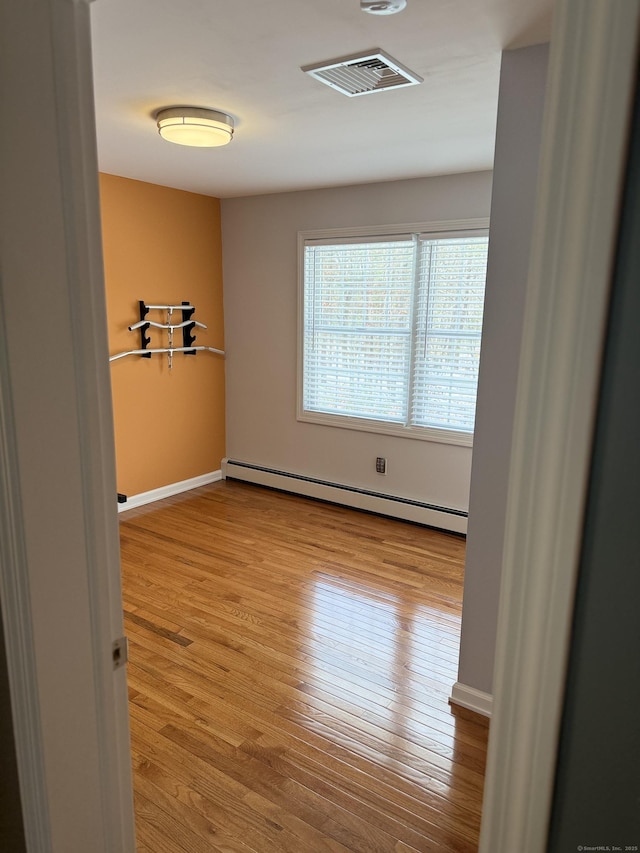 unfurnished room with a baseboard heating unit, wood finished floors, visible vents, and baseboards