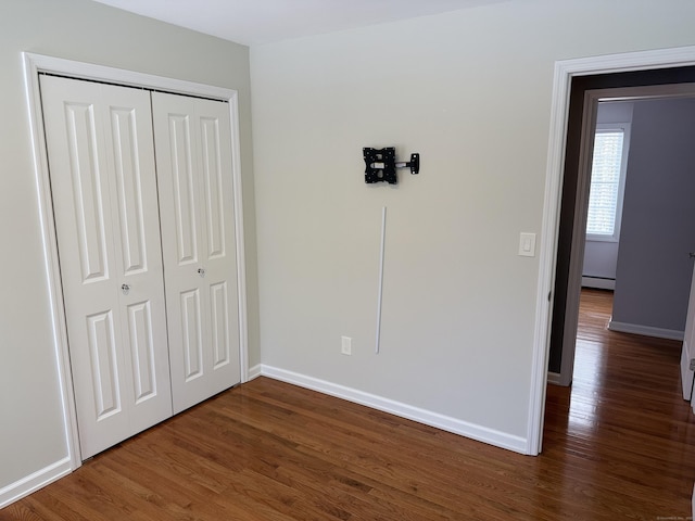 unfurnished bedroom with a closet, baseboards, baseboard heating, and dark wood-style floors