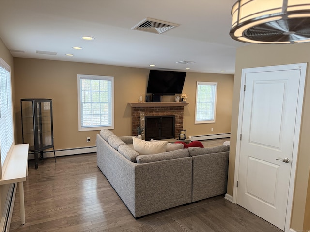 living room featuring a baseboard heating unit, wood finished floors, a fireplace, and visible vents