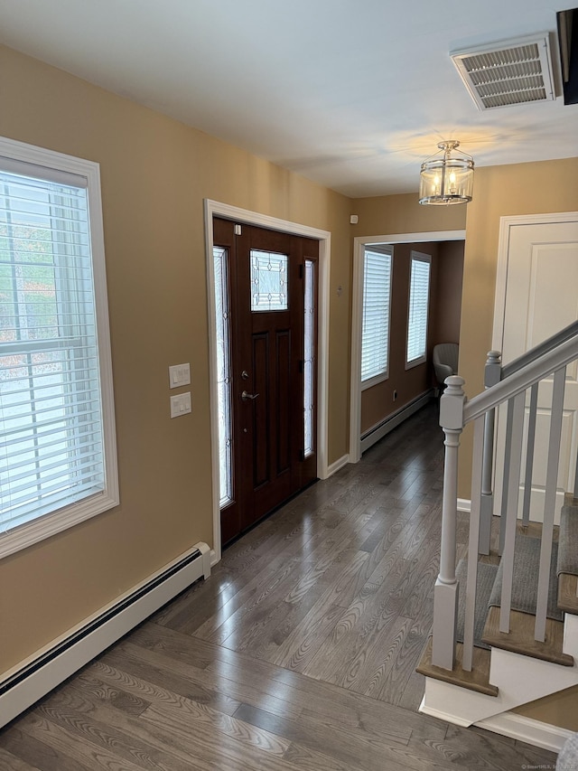 foyer with a wealth of natural light, visible vents, a baseboard heating unit, and wood finished floors