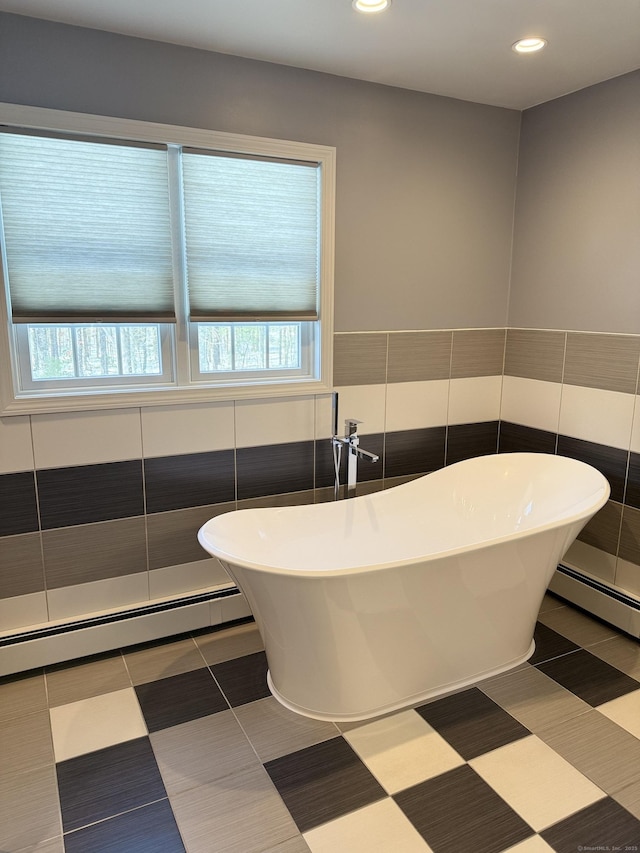 bathroom featuring a wealth of natural light, a freestanding bath, and a baseboard radiator