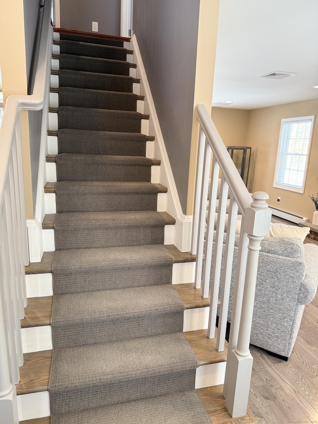 stairs with visible vents, baseboard heating, and wood finished floors