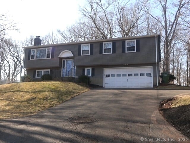 bi-level home featuring aphalt driveway, a front lawn, a chimney, and a garage