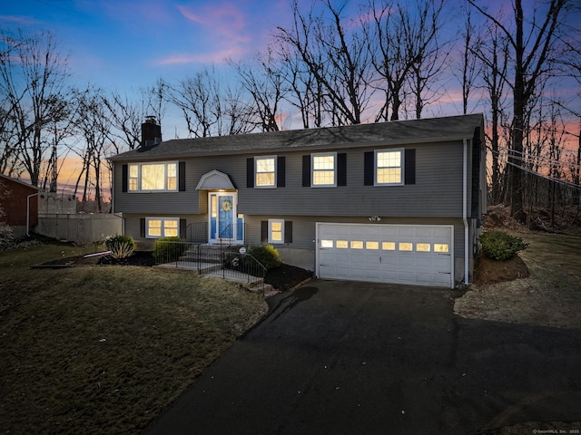 split foyer home featuring driveway, fence, a yard, an attached garage, and a chimney