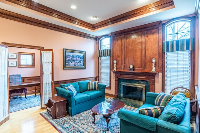 living area with light wood finished floors, a healthy amount of sunlight, a raised ceiling, and crown molding