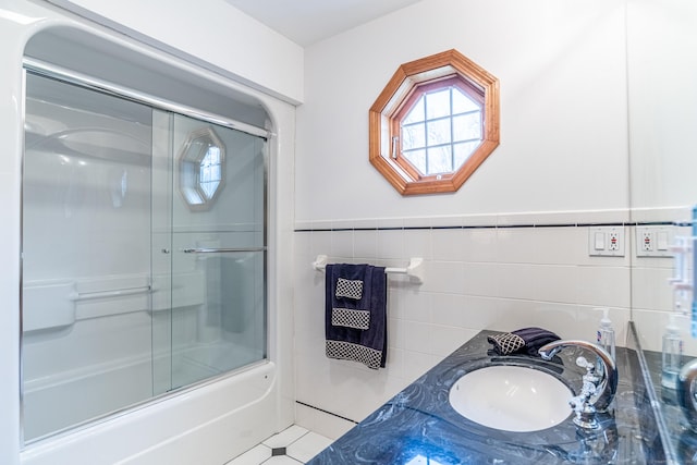 bathroom with tile patterned floors, a wainscoted wall, a sink, tile walls, and enclosed tub / shower combo