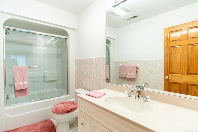 bathroom featuring visible vents, toilet, tile walls, enclosed tub / shower combo, and vanity