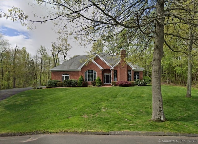 ranch-style home featuring brick siding, driveway, a chimney, and a front yard