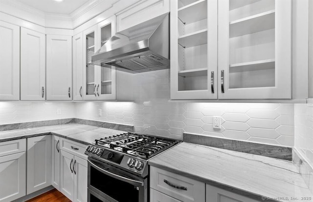 kitchen featuring glass insert cabinets, wall chimney exhaust hood, light stone countertops, and stainless steel gas stove