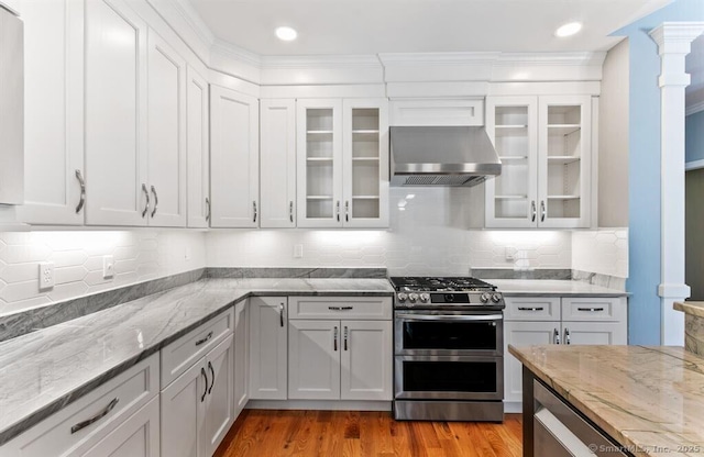 kitchen with range with two ovens, light stone counters, light wood-style flooring, white cabinetry, and wall chimney exhaust hood