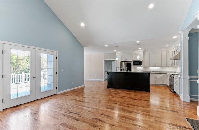 kitchen with light wood finished floors, under cabinet range hood, decorative columns, appliances with stainless steel finishes, and white cabinets