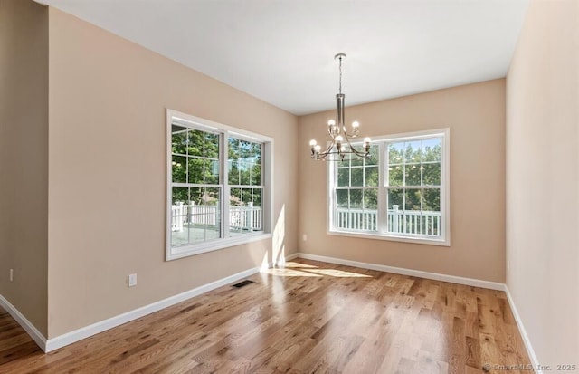 unfurnished dining area featuring visible vents, a notable chandelier, wood finished floors, and baseboards