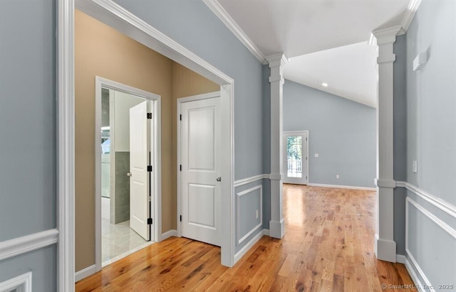 hall featuring light wood-type flooring, ornamental molding, baseboards, decorative columns, and lofted ceiling