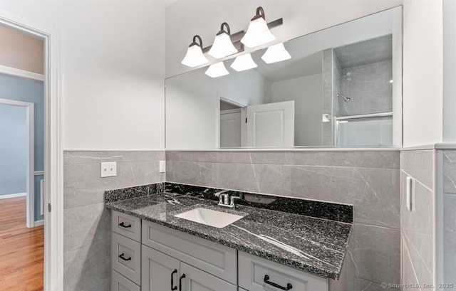 full bathroom featuring vanity, wainscoting, wood finished floors, tile walls, and a shower