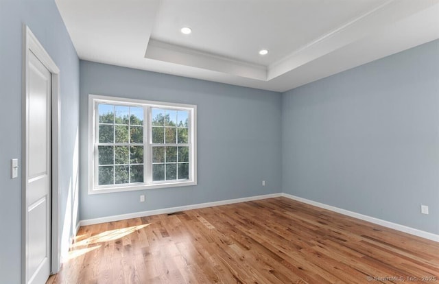 unfurnished room featuring recessed lighting, baseboards, a raised ceiling, and wood finished floors